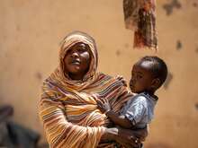 Woman holding a child against backdrop of destroyed building